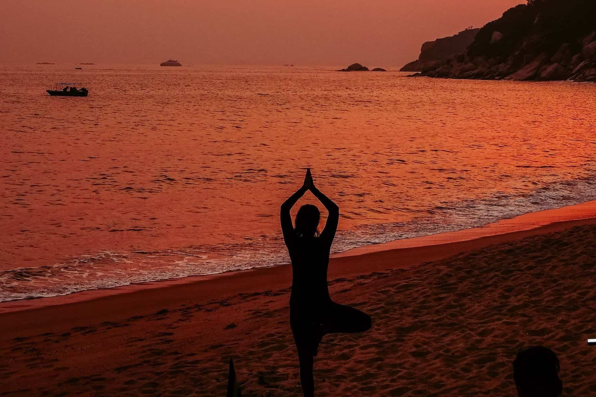 woman practicing yoga on the beach at sunset